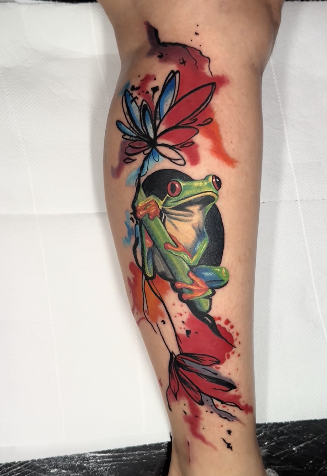 Watercolor red-eyed tree frog calf tattoo with red and blue splashes